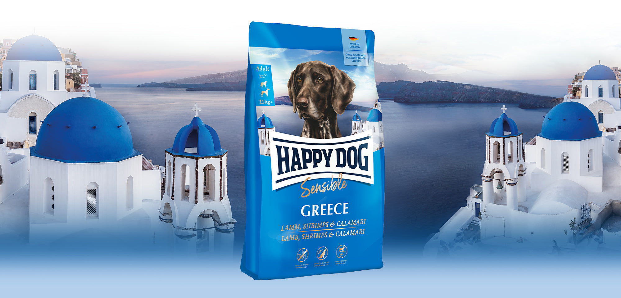 Das Hundefutter Happy Dog Sensible Greece, abgebildet vor einer typisch griechischen Inselkulisse mit weiß-blauen Häusern.